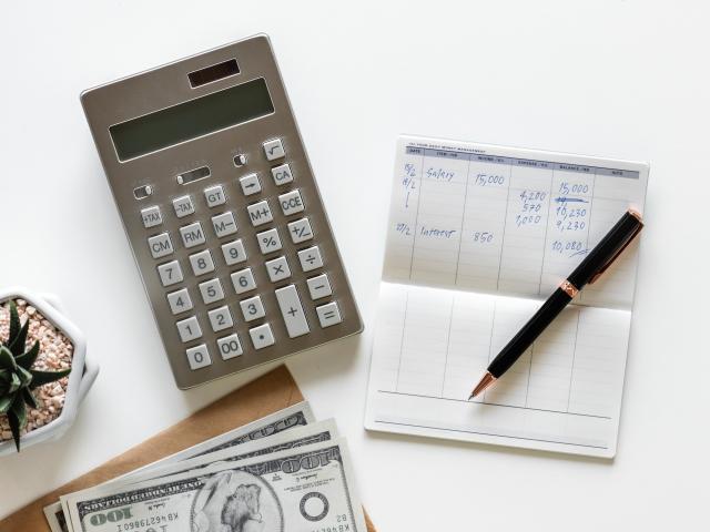 A calculator, bank balance booklet, pen, cash, and desktop plant.