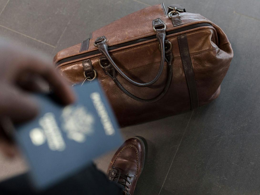 A hand, holding a passport, reaches from outside the frame toward a packed travel bag
